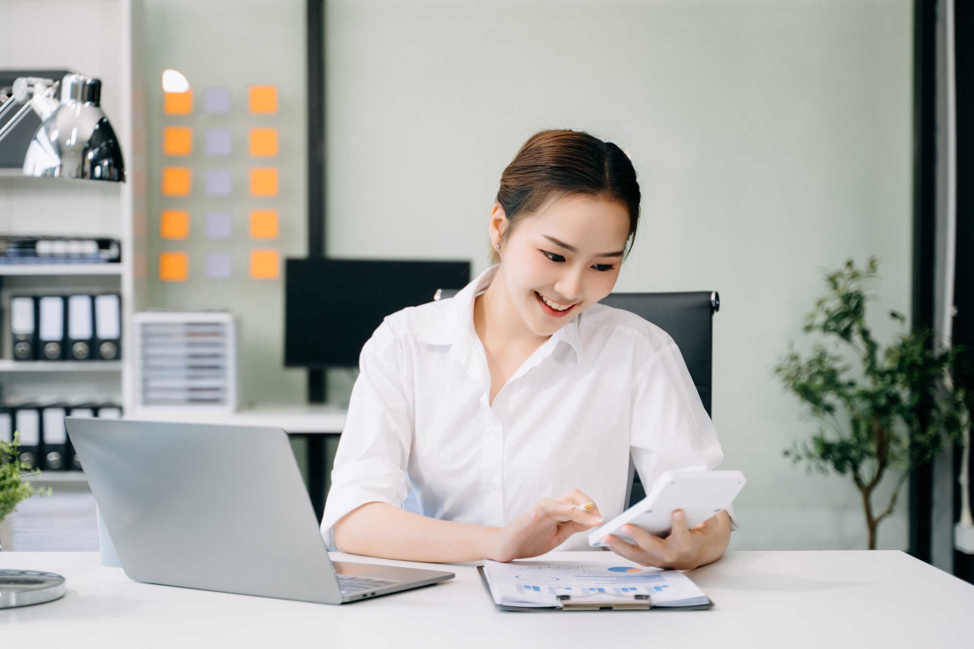 Asian Businesswoman Analyzing Finance on Tablet and Laptop at Office Desk tax, report, accounting,