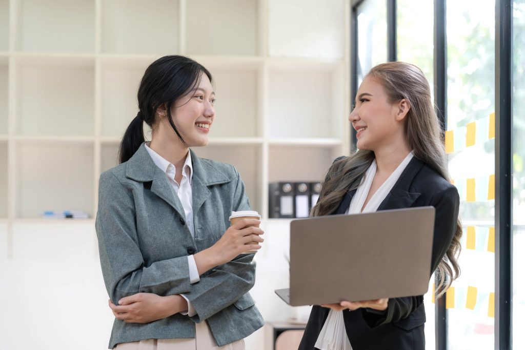 Two beautiful Asian businesswomen standing using digital tablet consulting and analyzing information